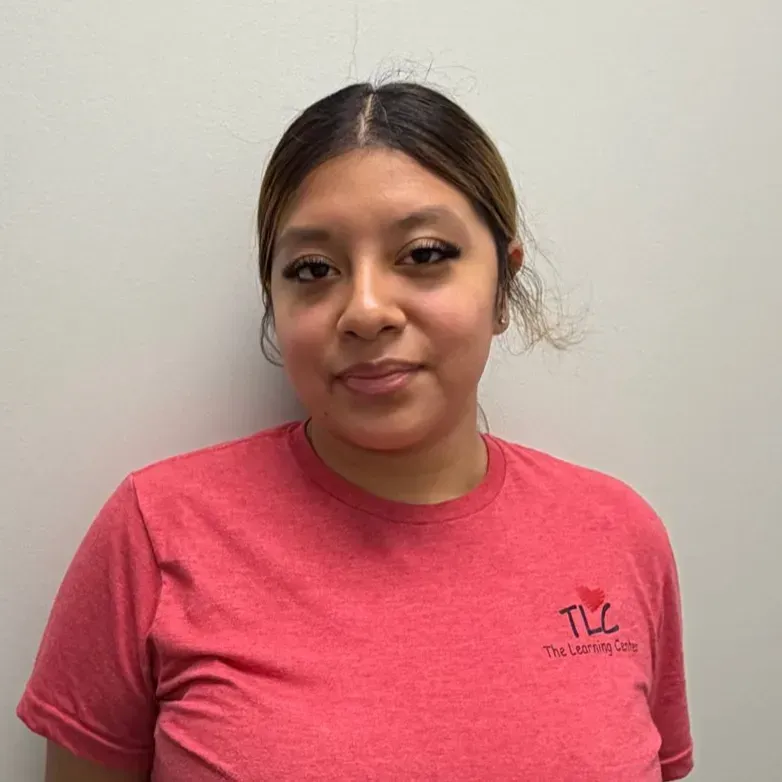 Woman wearing a red shirt with a logo, in front of a neutral wall.