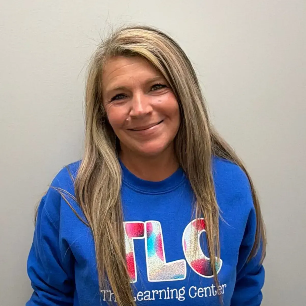 Woman with long blonde hair smiles, wearing a blue sweatshirt with 