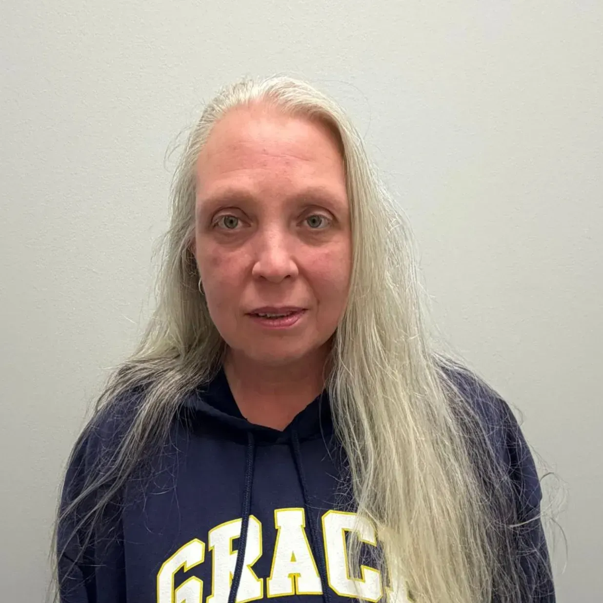 Woman with long gray hair wearing a navy hoodie, looking forward against a gray wall.