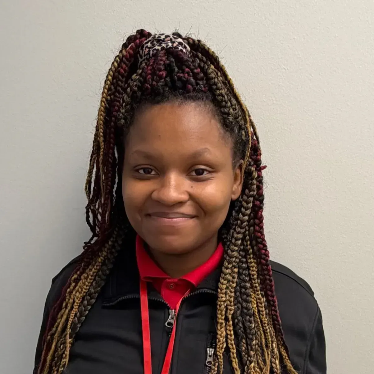 Woman with braided hair smiling, wearing a black jacket over a red polo, and a lanyard.