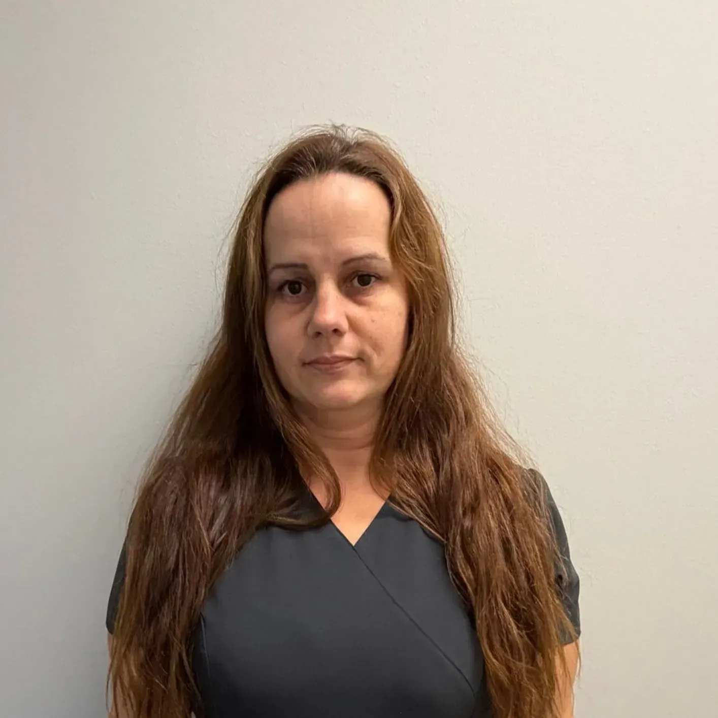 Woman with long brown hair, wearing a dark top, against a plain background.