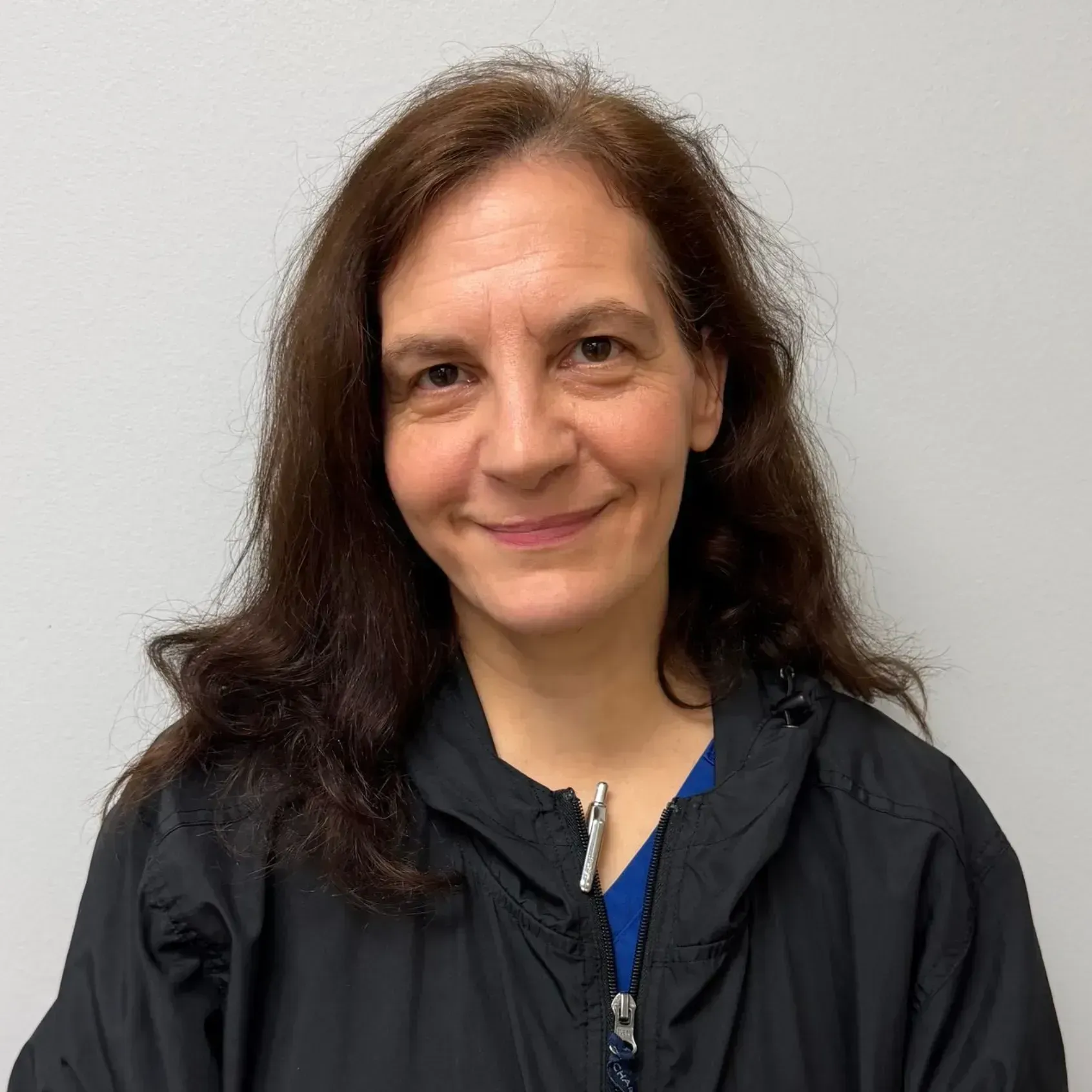 Woman with dark hair smiles, wearing a black jacket and blue top, against a white background.