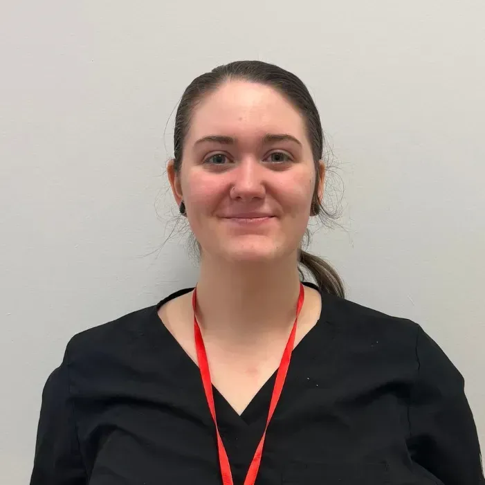 Woman with dark hair in black top and red lanyard, smiling at the camera.