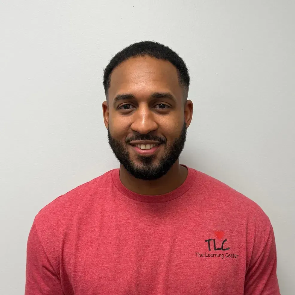 Man with short hair and beard smiles, wearing a red shirt with 