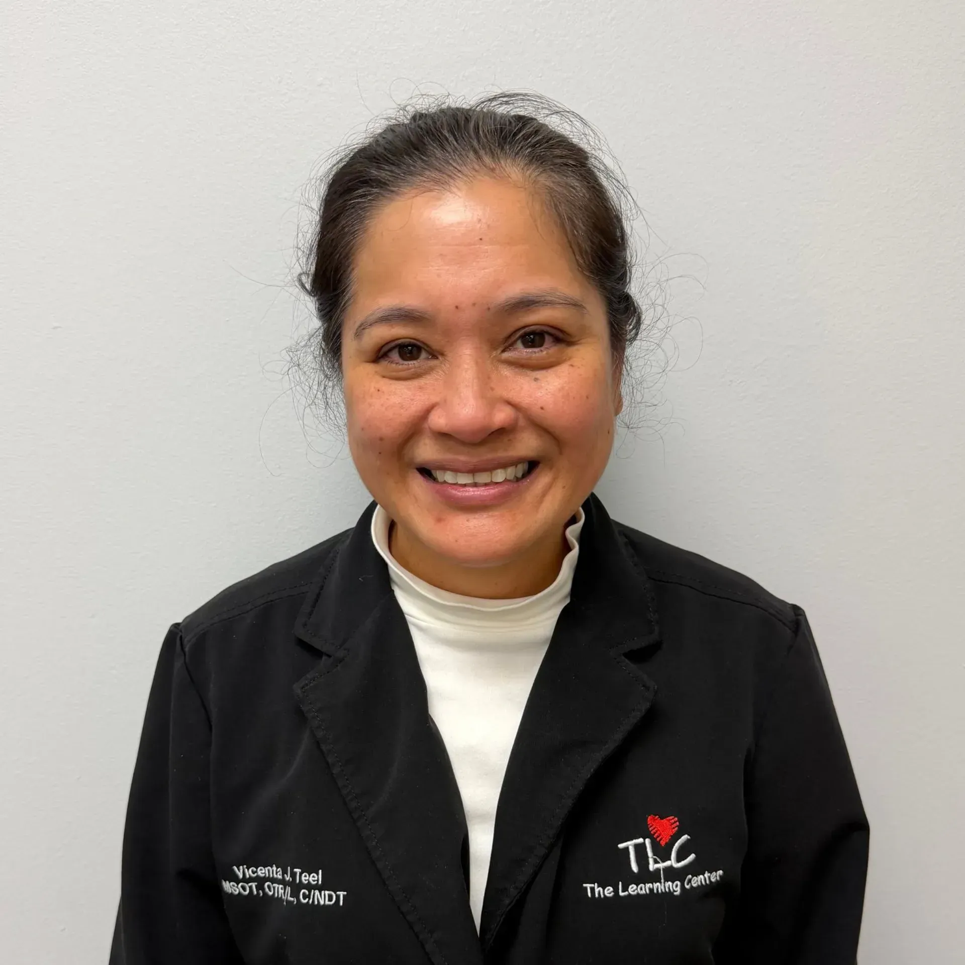 Woman smiling, wearing black jacket over white shirt. The Learning Center logo is visible.