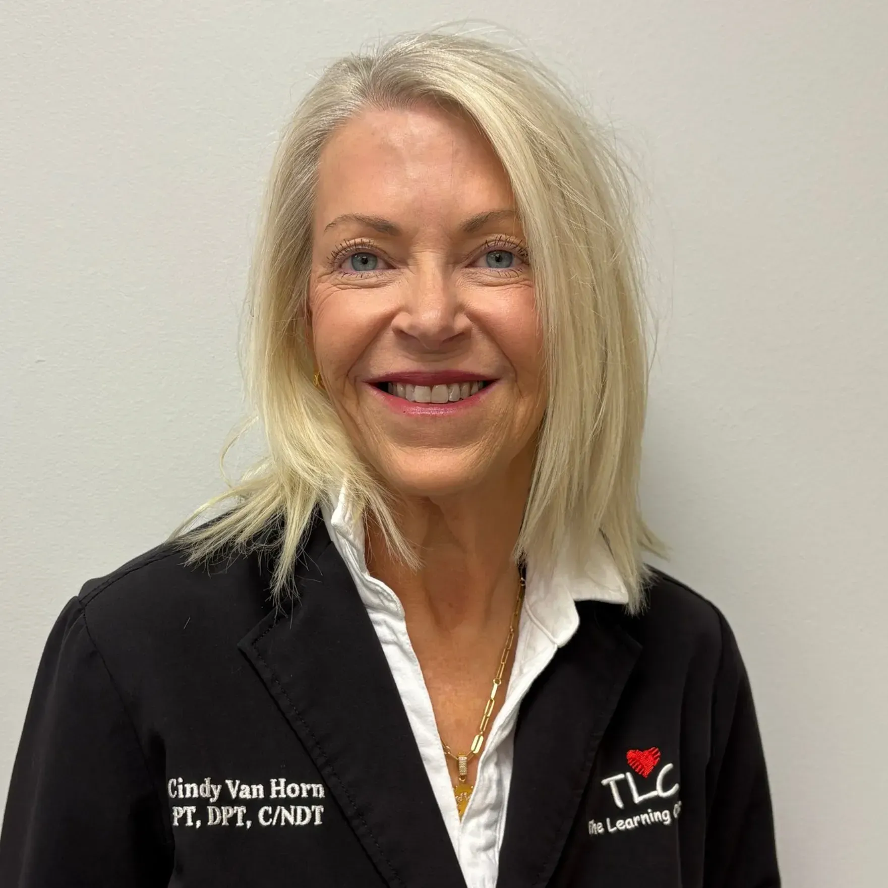 Woman with blonde hair, wearing a black jacket and white collared shirt, smiling at the camera. TLC logo.