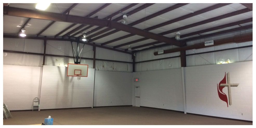 An empty gym with a basketball hoop and a cross on the wall.