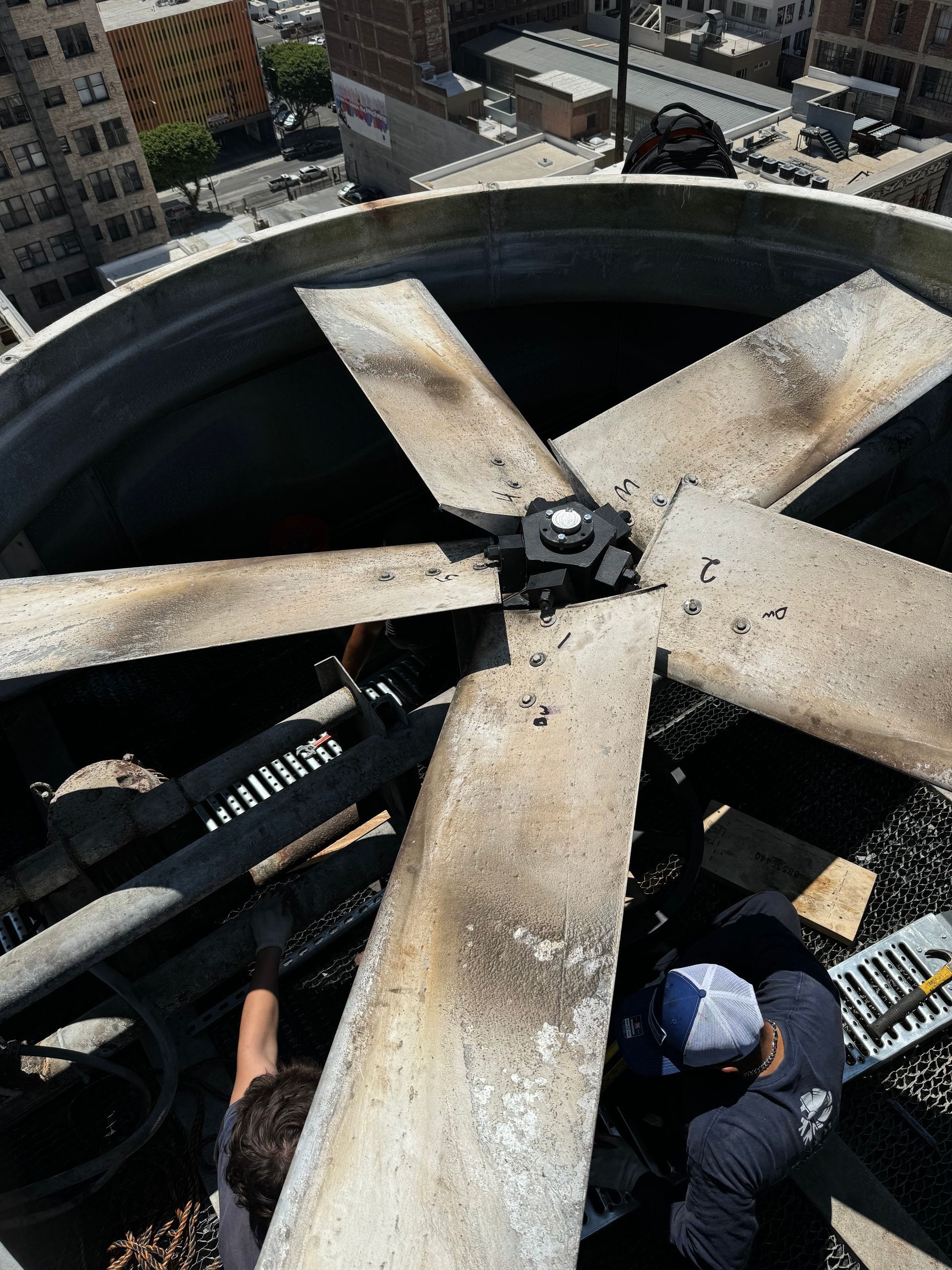 Two men are working on a large fan on top of a building