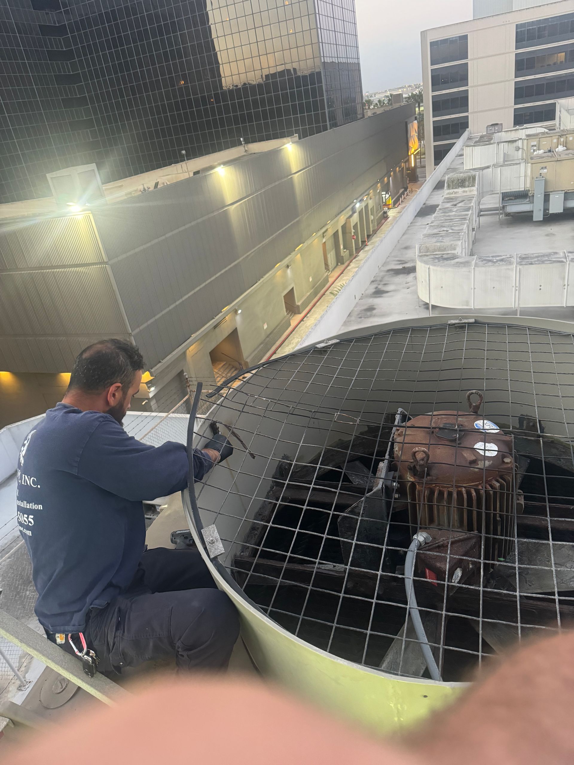 A man is working on a large fan on top of a building.