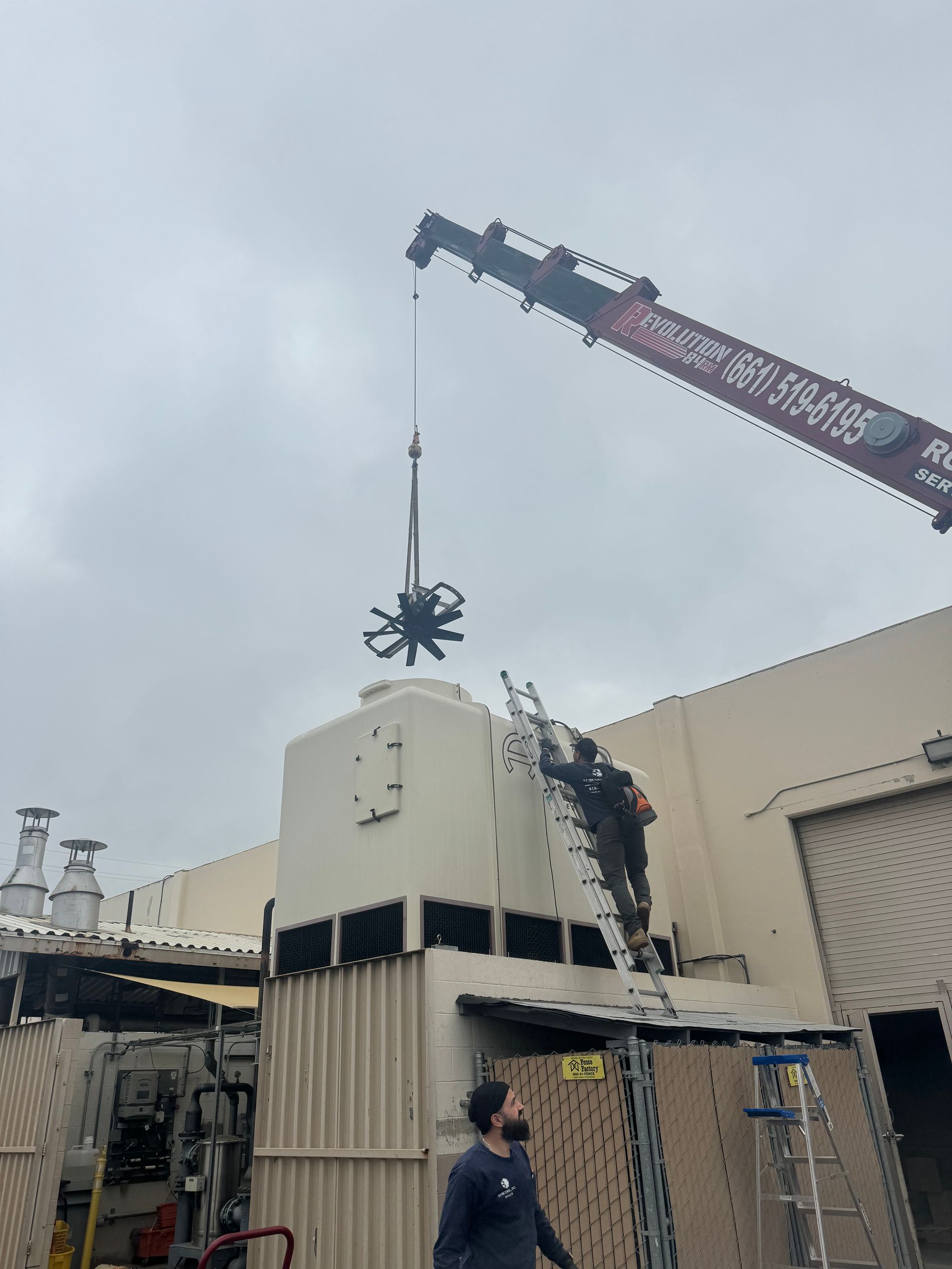 A man is standing on a ladder next to a crane lifting a machine.