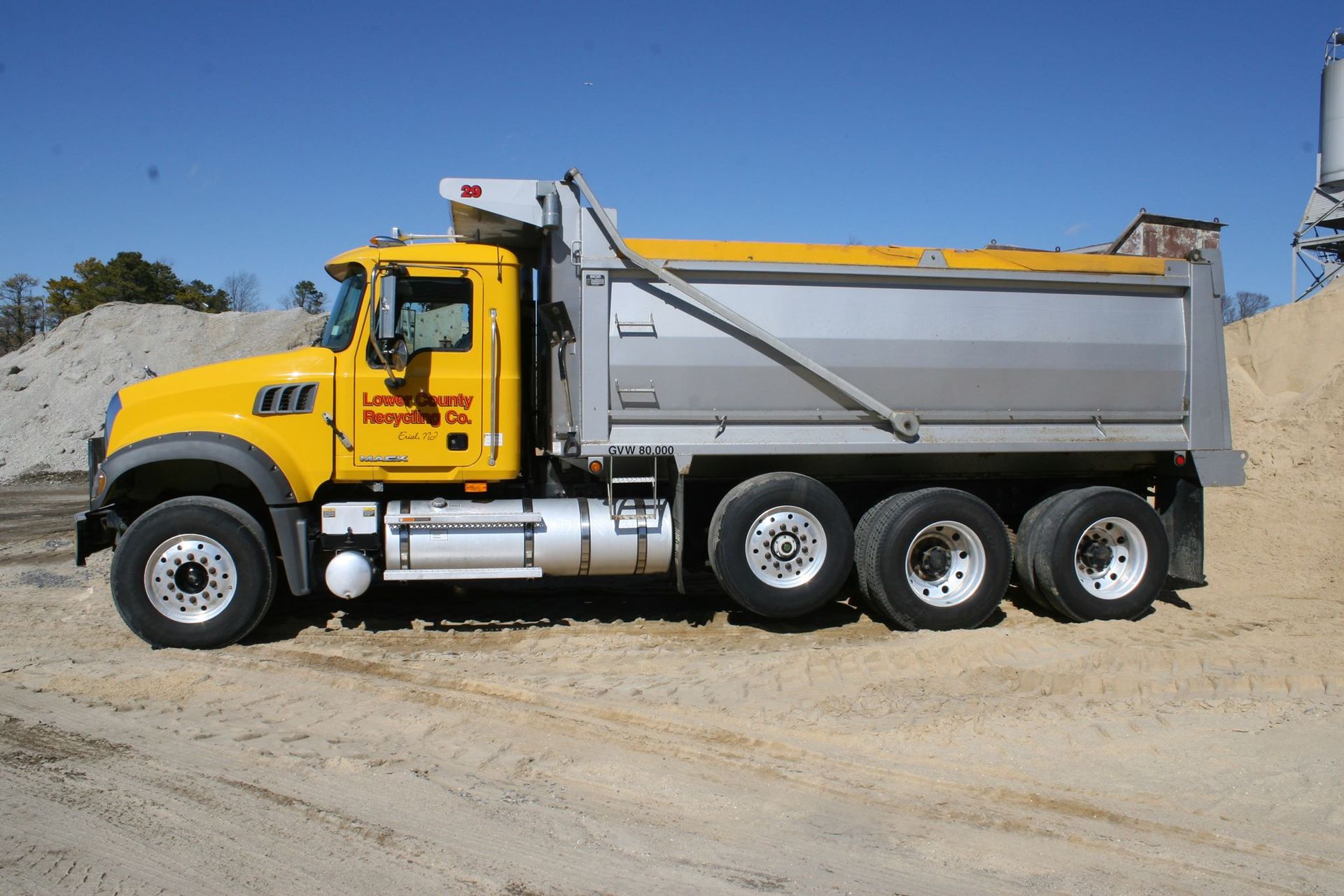 A yellow dump truck is parked in front of a pile of dirt.