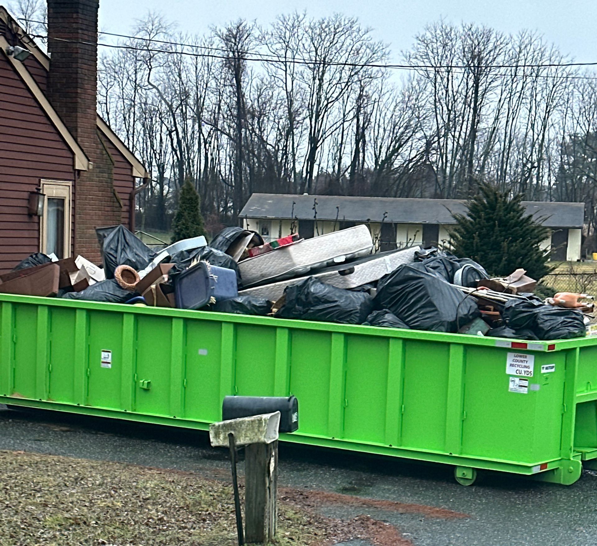 A green dumpster filled with trash is parked in front of a house.