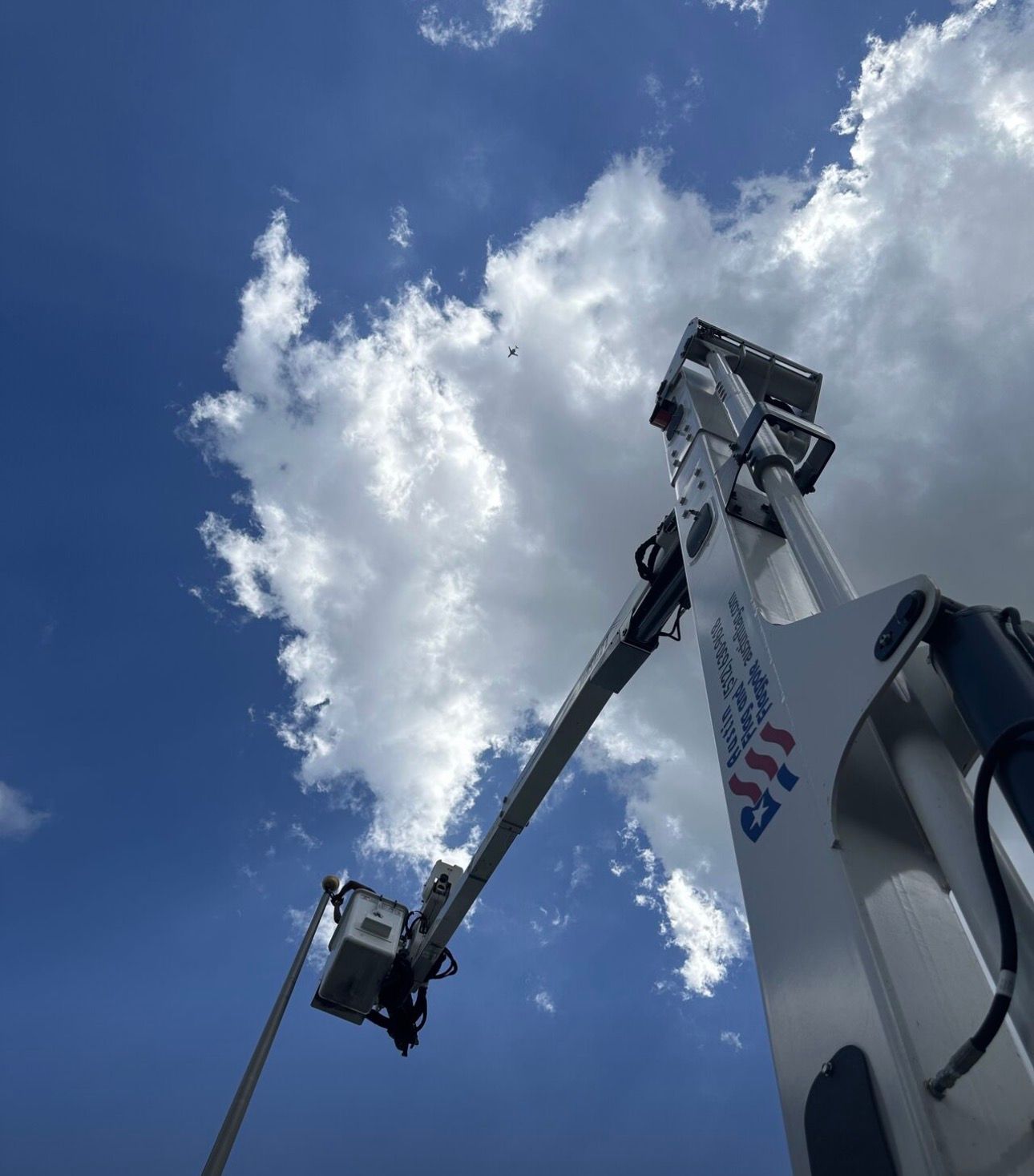 A utility truck boom reaching toward a cloudy sky. The truck is white with red and blue accents.