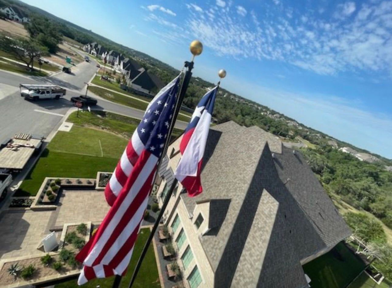 American and Texas flags flying against a blue sky, above a residential area.