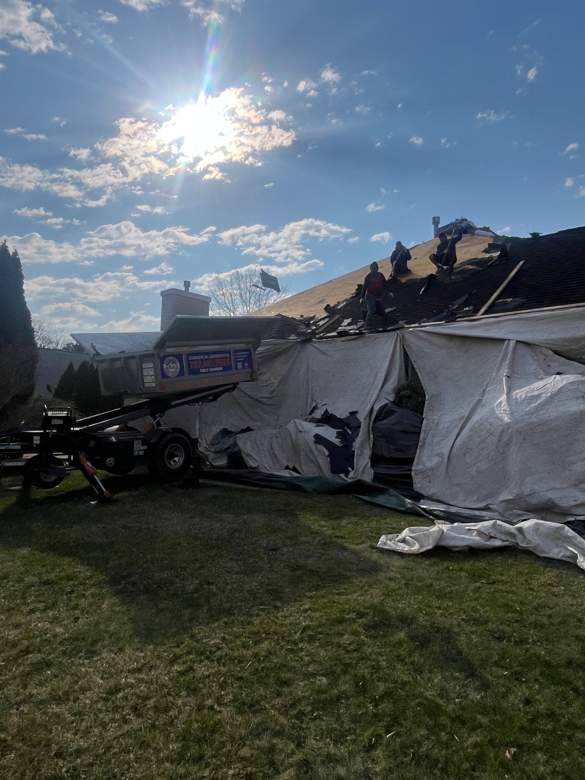 Workers on the roof of a building under renovation, with white protective tarps draped over the exterior wall.
