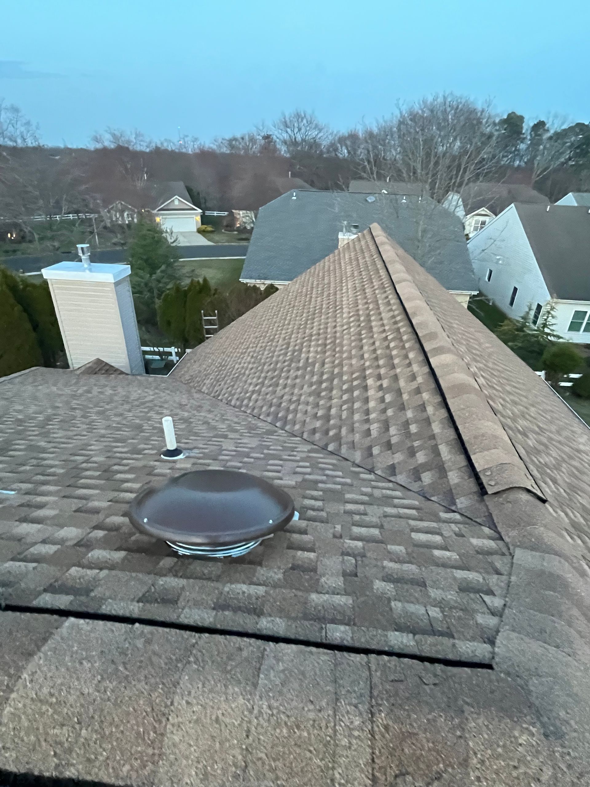 High-angle view of a brown asphalt shingle roof featuring a circular roof vent and a white chimney.