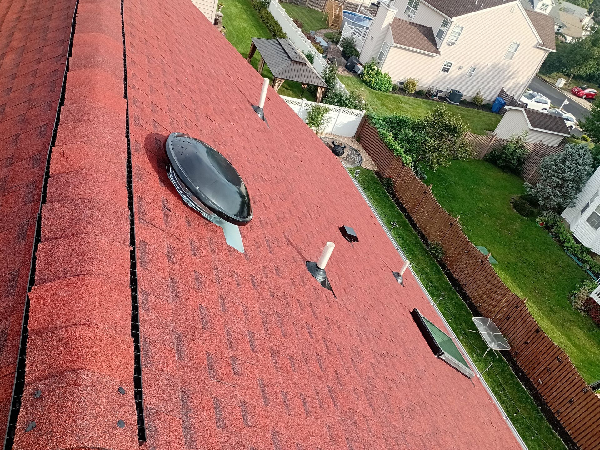 Tilted view of a red roof overlooking neighboring houses and green yards.