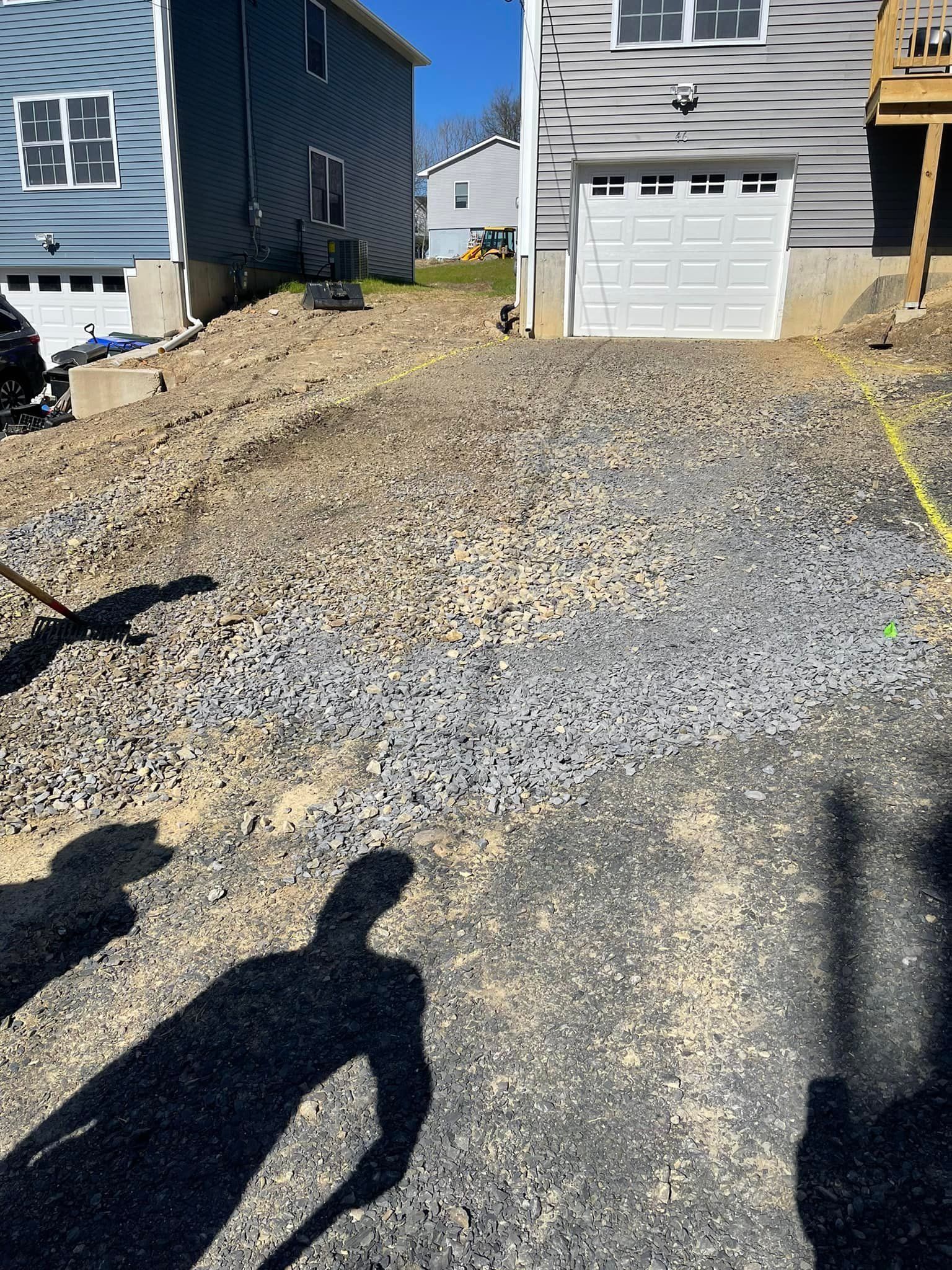 newly paved driveway with grass on both sides and gray house at the back