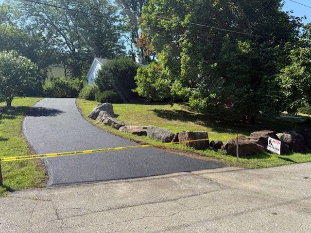 A newly paved driveway is surrounded by trees and grass.