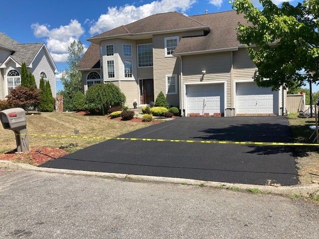 newly paved driveway with cream colored house and white garage