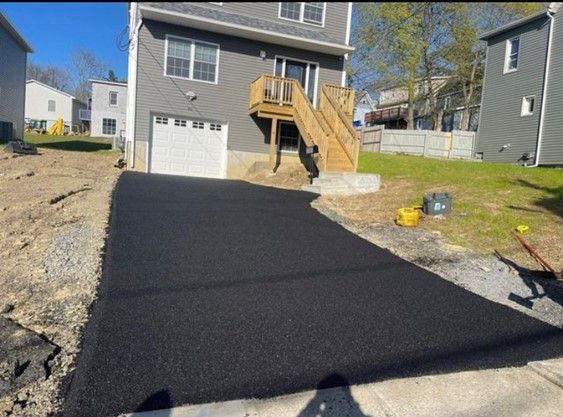 newly paved driveway with gray house in the background