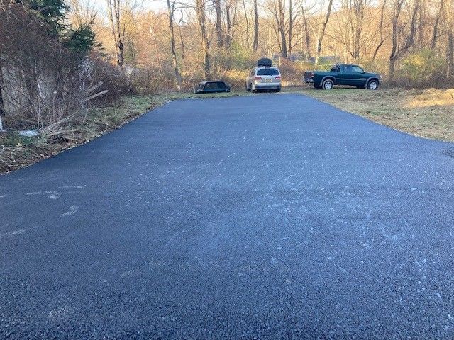 asphalt driveway with three vehicles in the background
