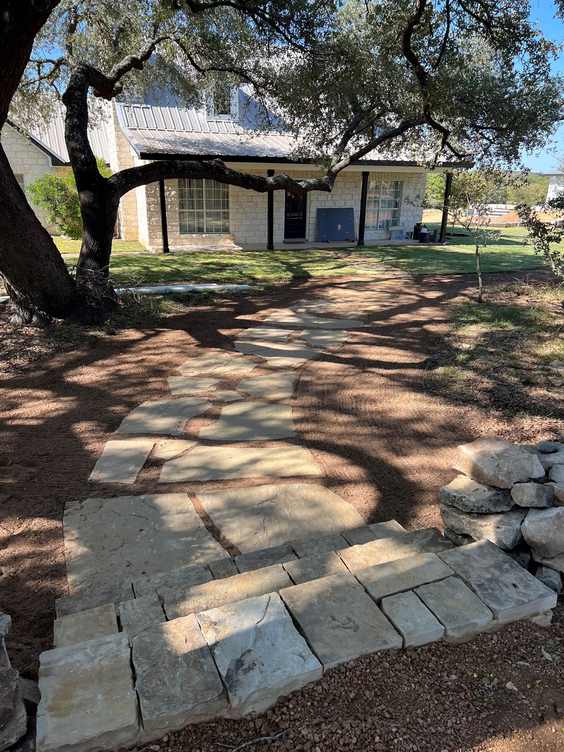 A stone walkway leading to a house with a tree in the background.