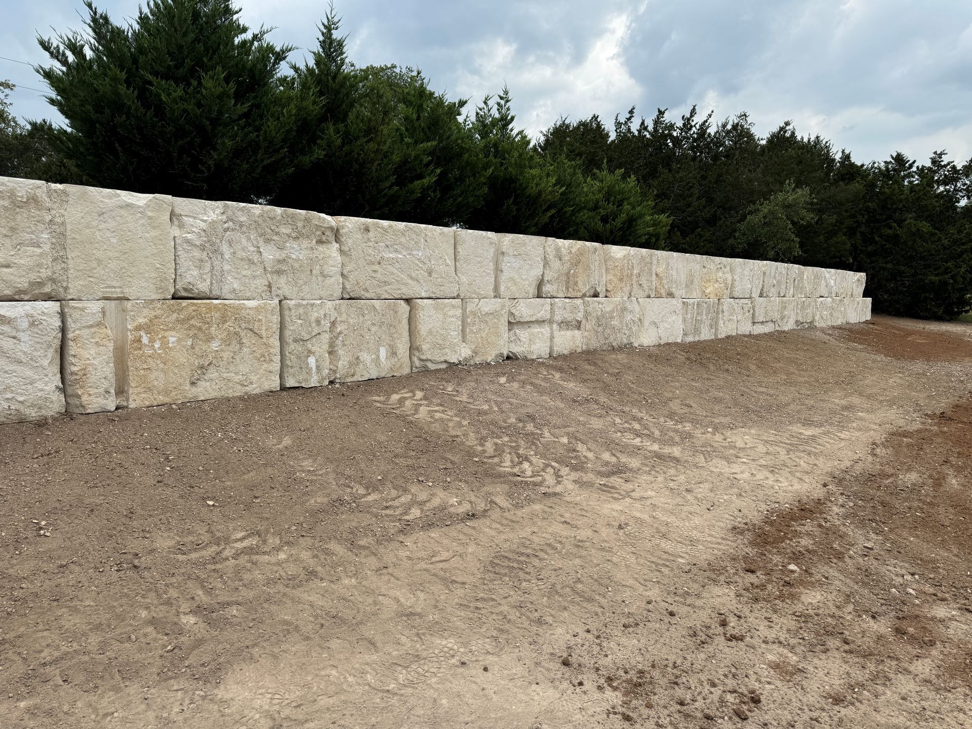 A large stone wall is sitting in the middle of a dirt field.