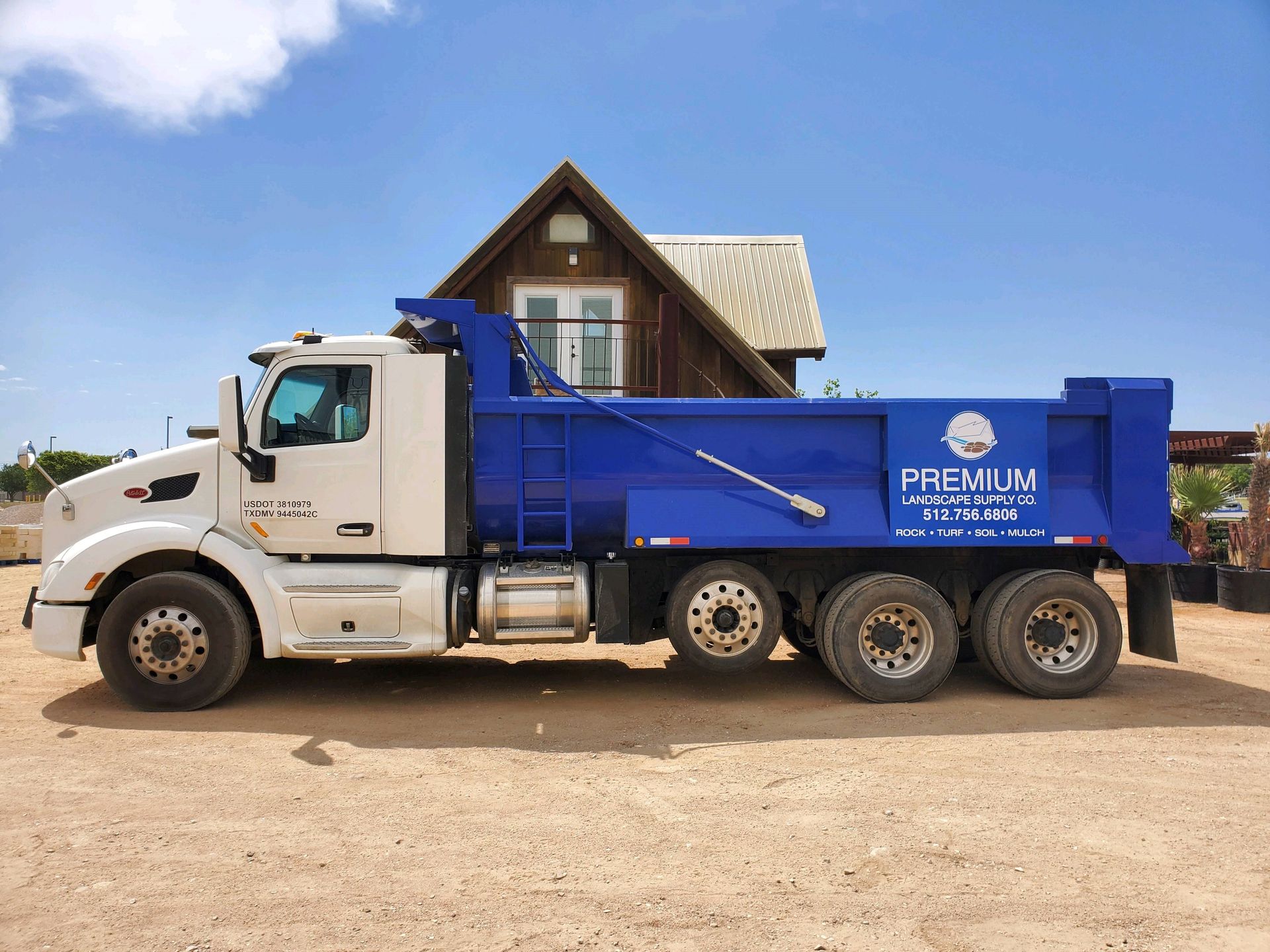 White and blue dump truck parked in front of a house on a sunny day.