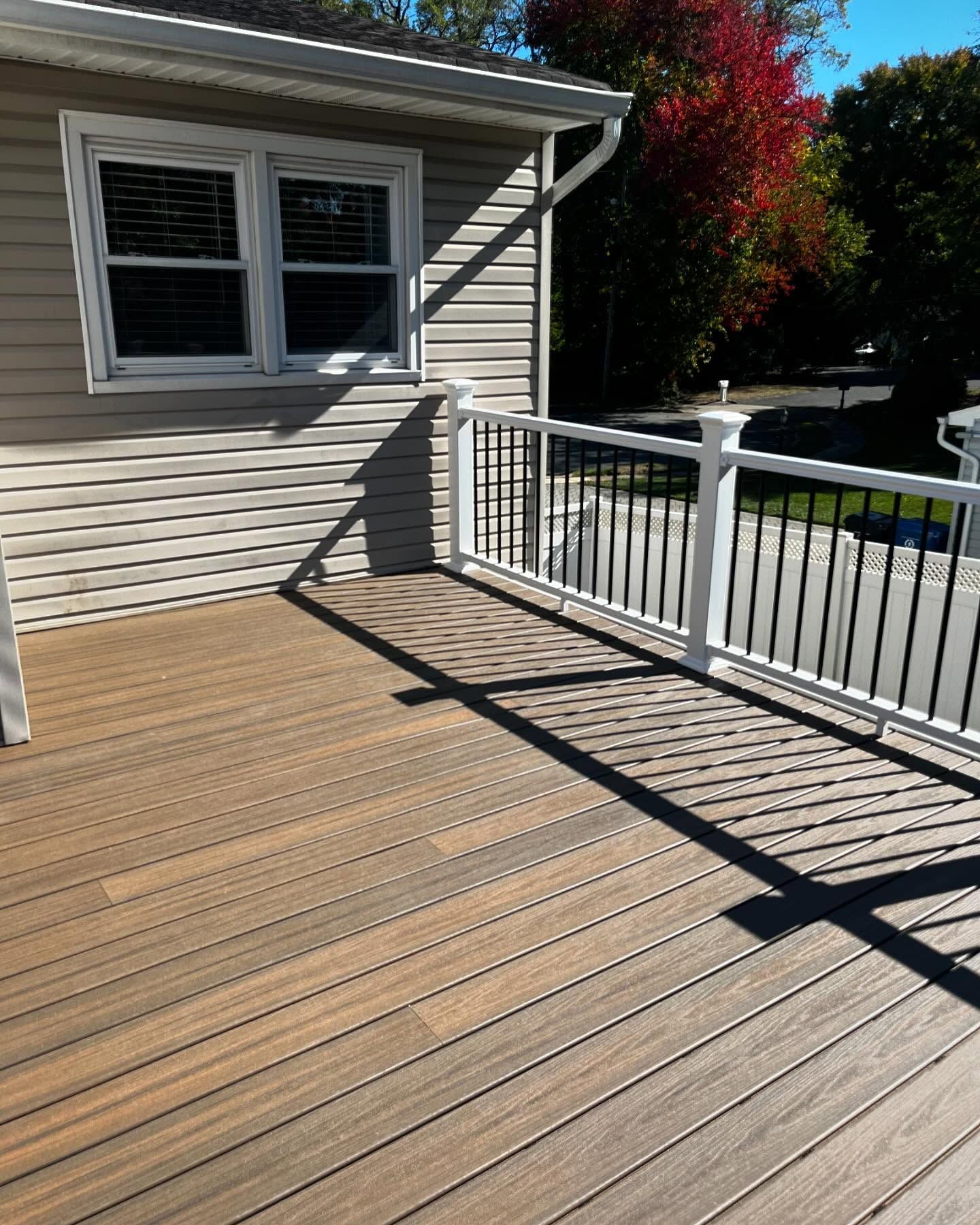 A composite deck with a white railing and black spindles, attached to a house with beige siding.
