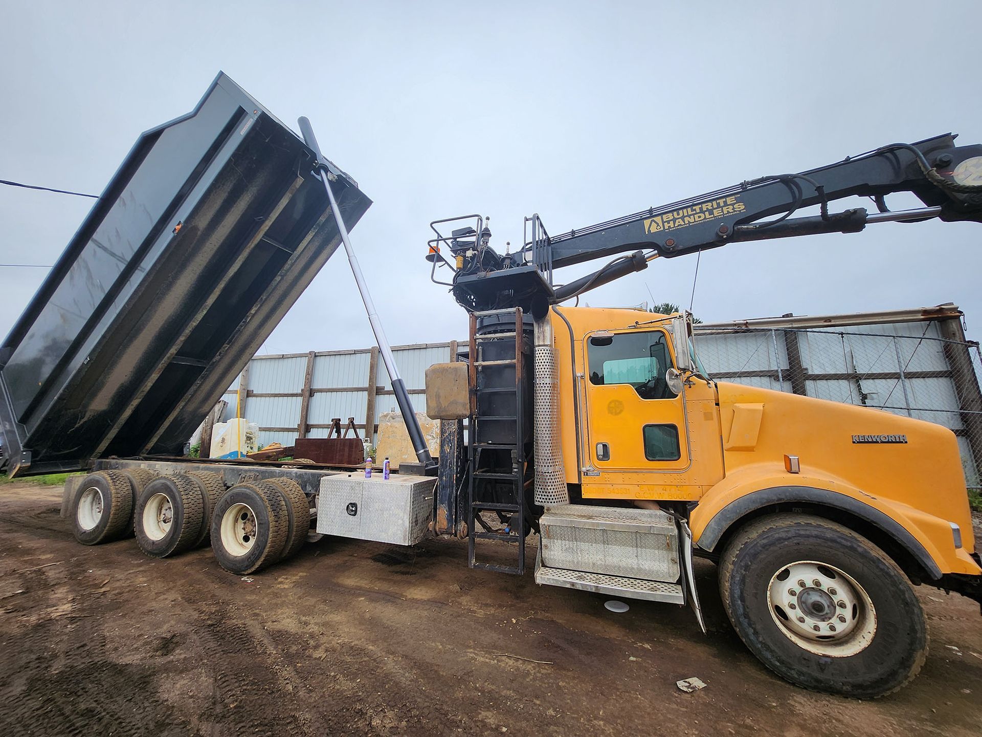 A dump truck with a crane attached to it is being loaded with dirt.