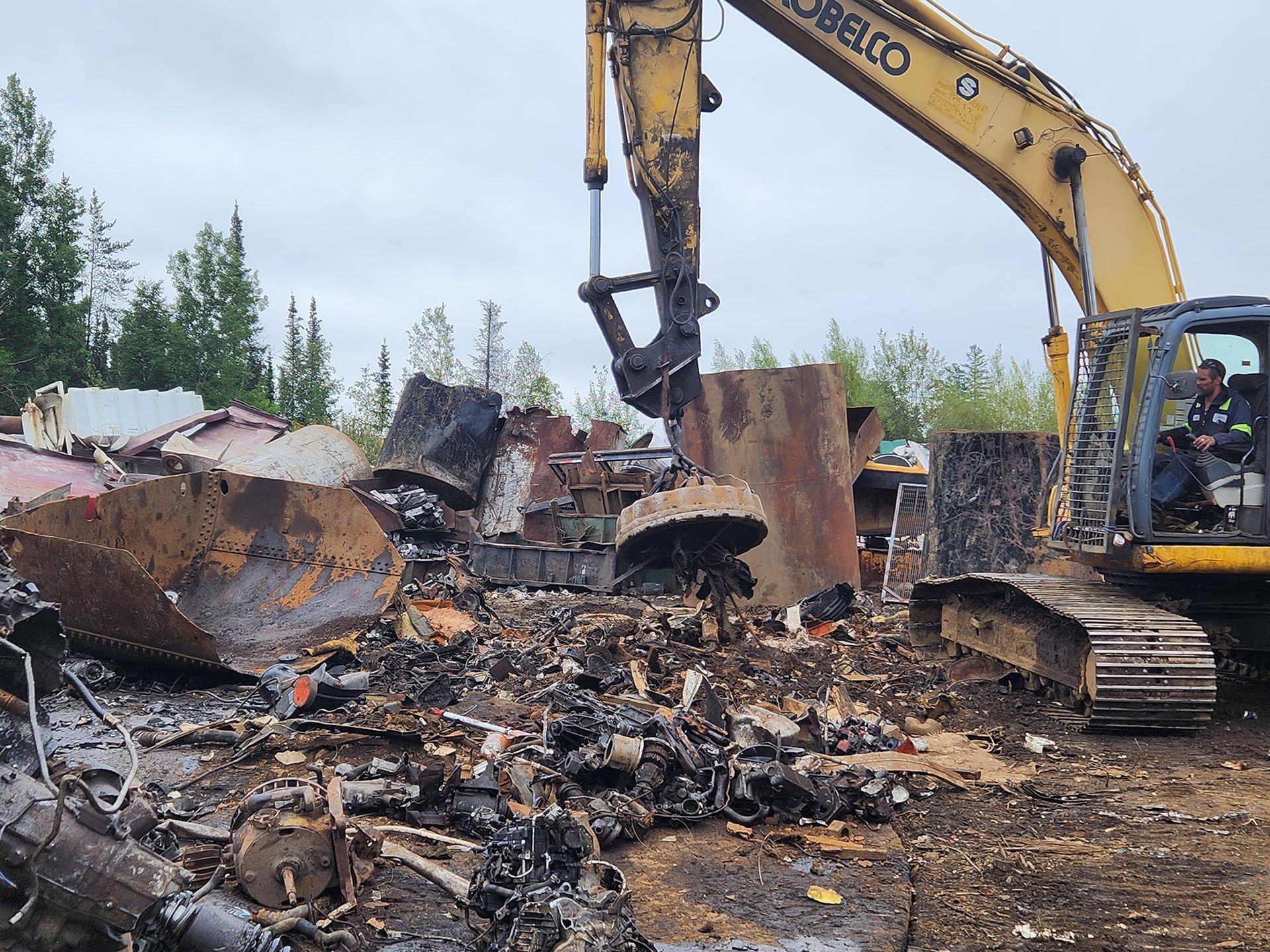 A yellow excavator is working on a pile of scrap metal.