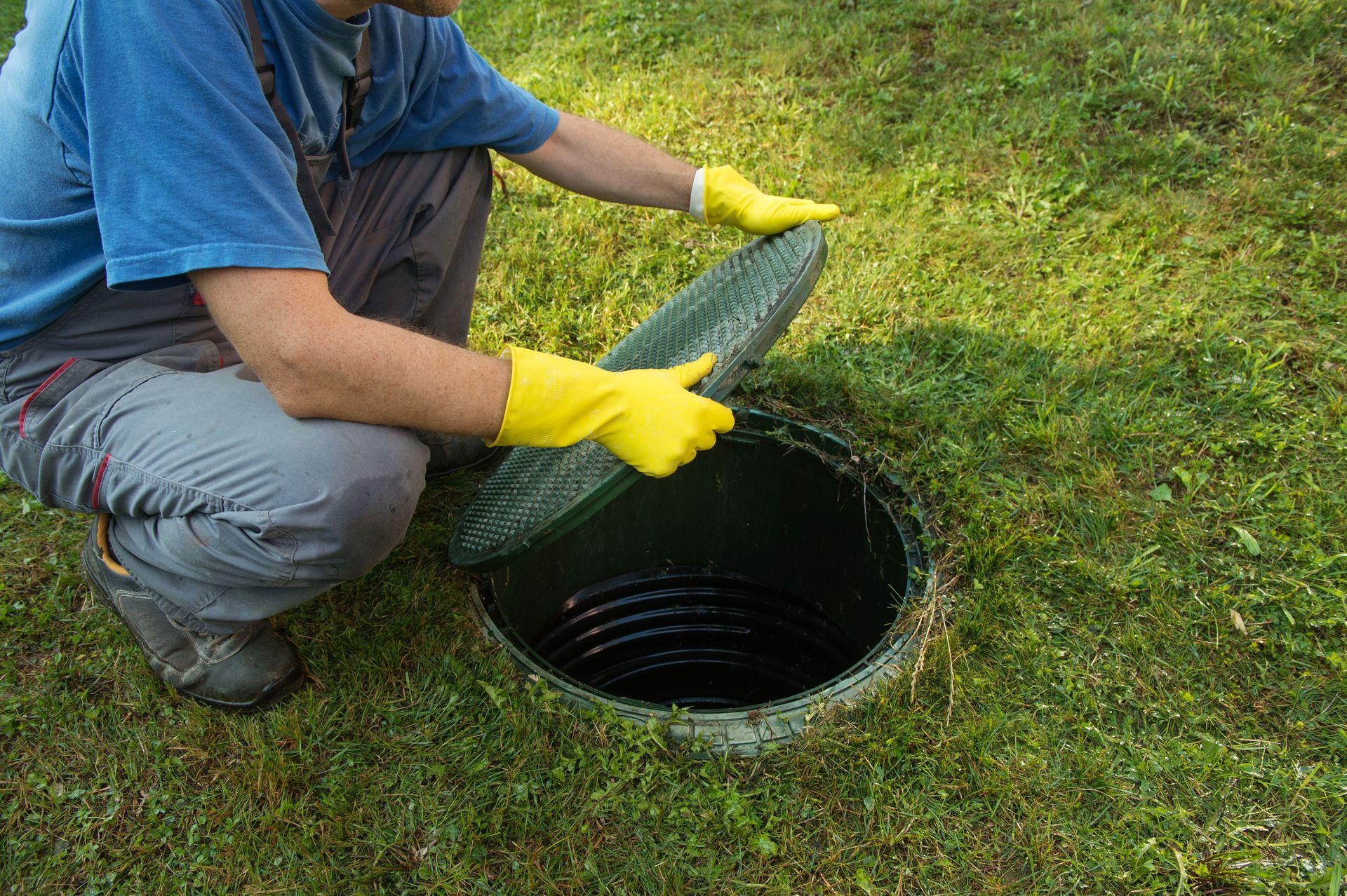 Person in yellow gloves lifting a green cover from a lawn drain hole.