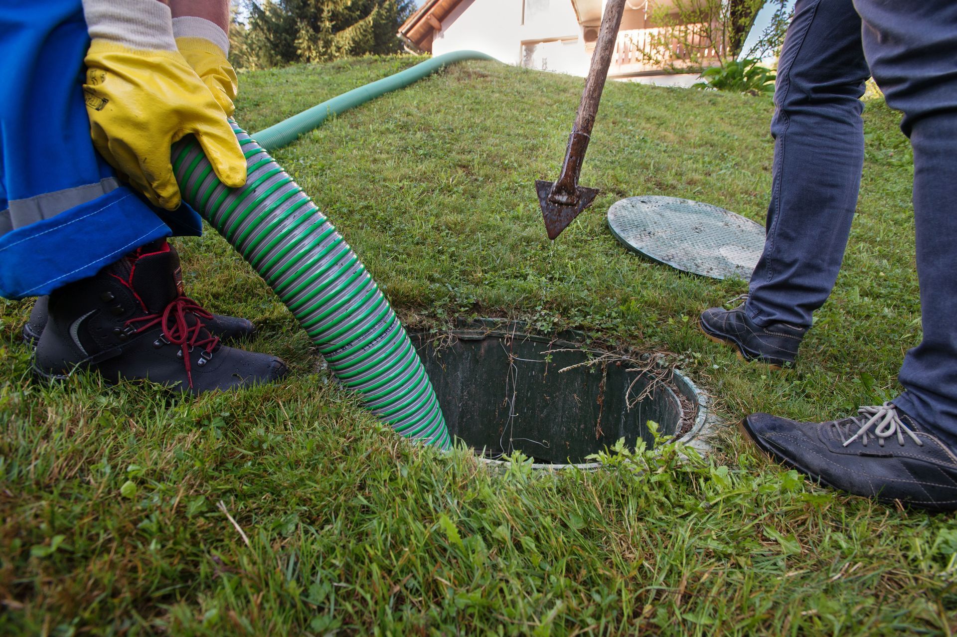Workers using a green hose to clean a lawn septic tank opening