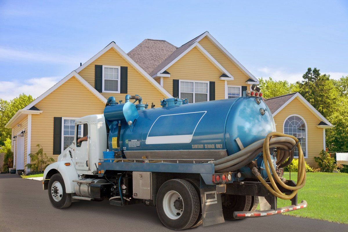 Blue septic truck parked in front of a yellow suburban house on a sunny day