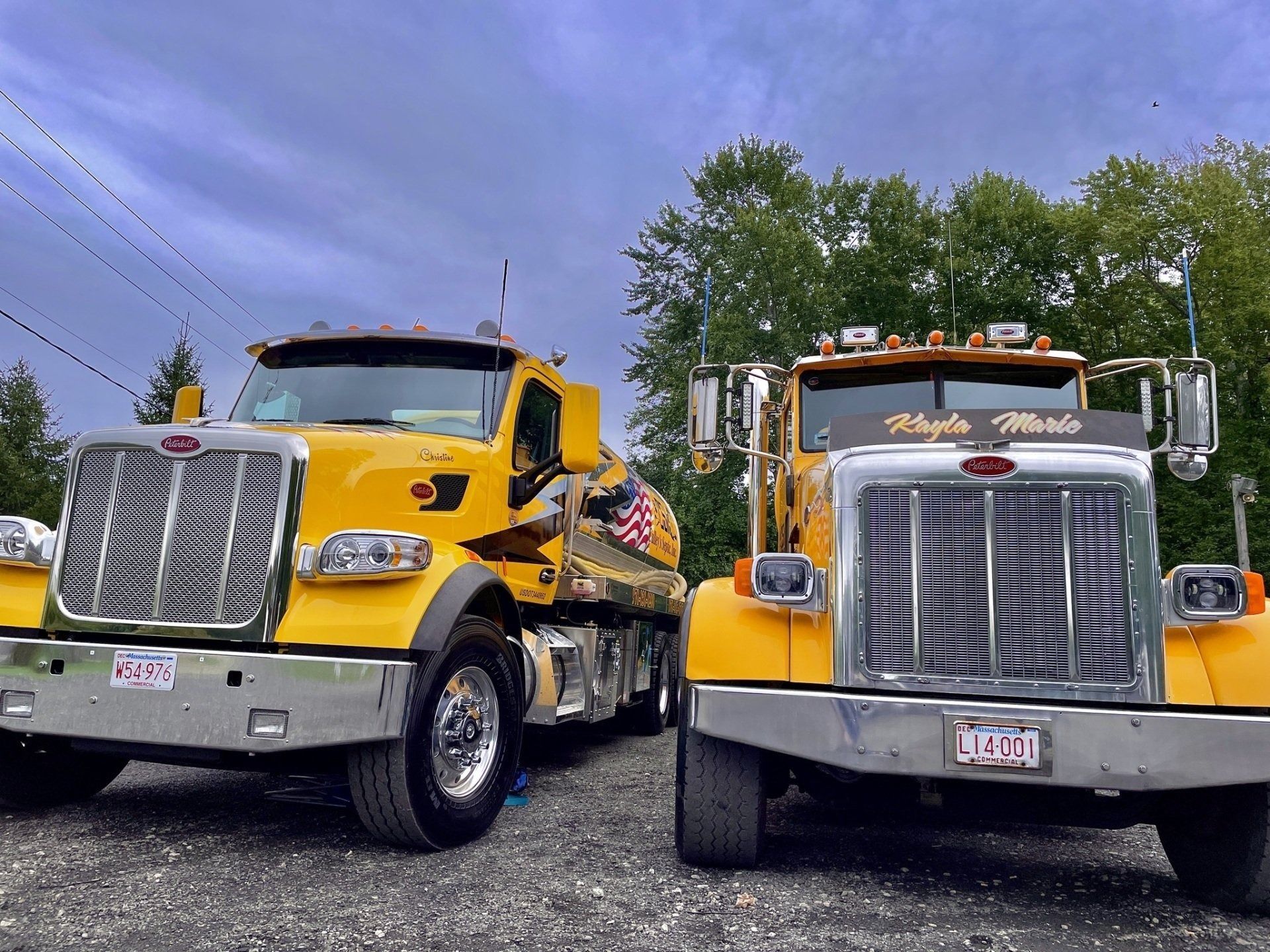 Two yellow dump trucks parked side by side on a lot under a cloudy sky