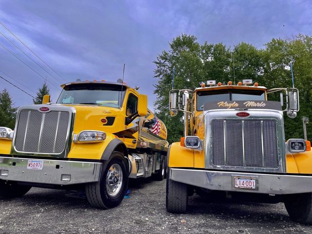 Two yellow dump trucks parked side by side on a lot under a cloudy sky
