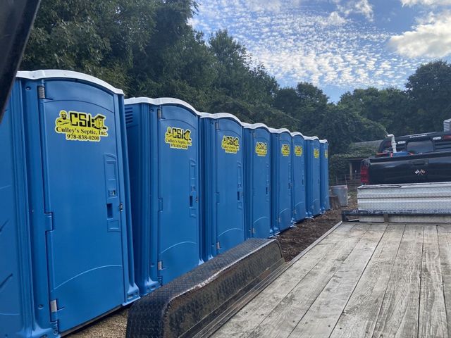Row of blue portable toilets along a wooden deck at an outdoor worksite under a cloudy sky