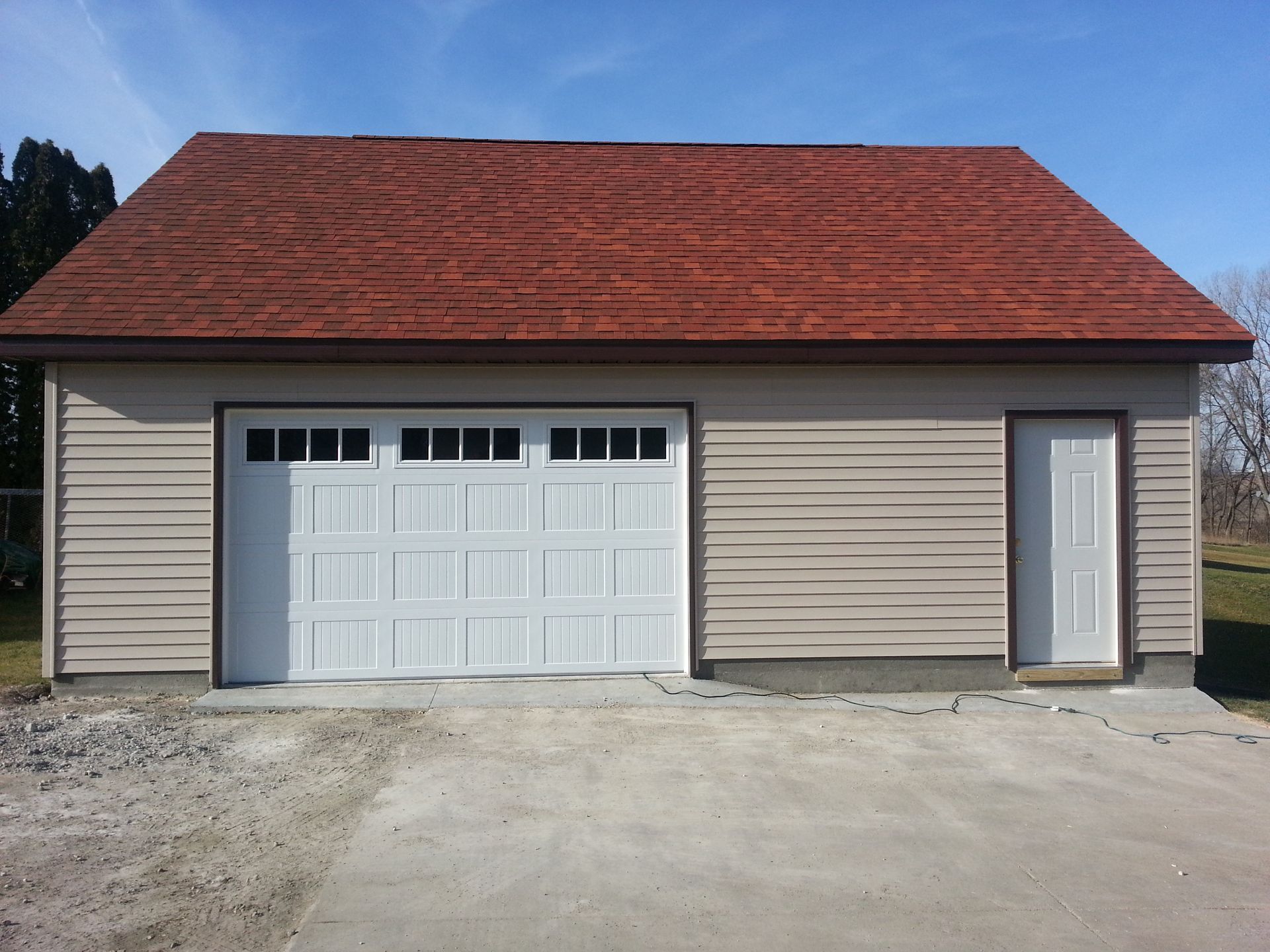 Detached beige garage with red roof, white door, and side entry door on a concrete driveway
