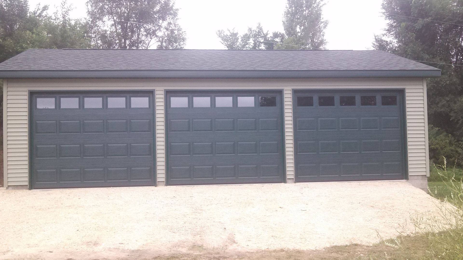 Three-car garage with dark gray doors and a light roof beside a gravel driveway.