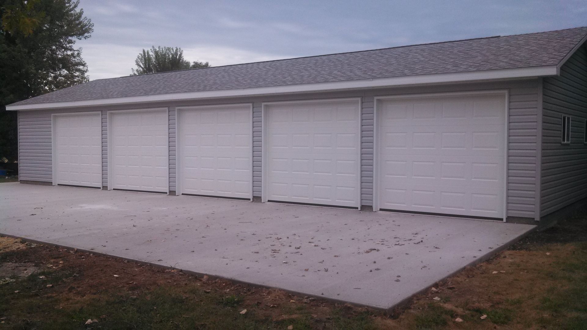 Row of four white garage doors on a light gray detached building with a concrete driveway in front