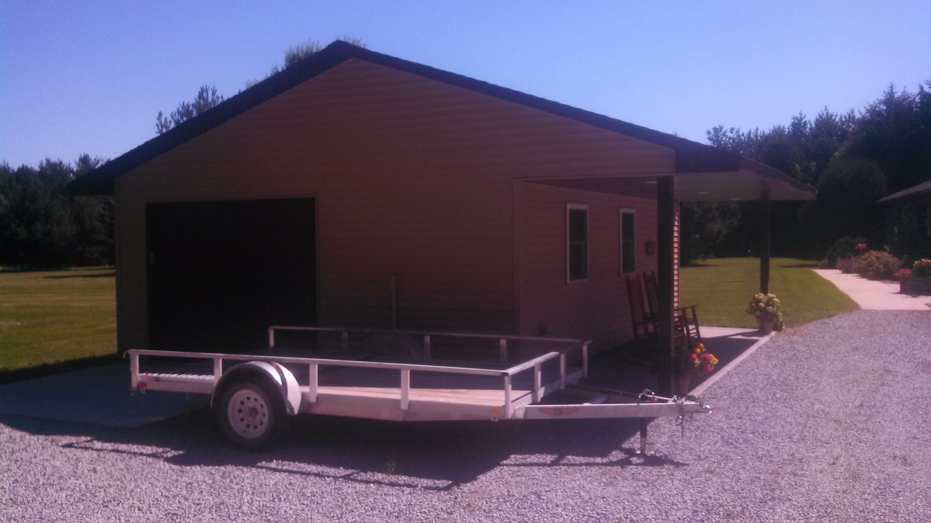 Brown shed on a gravel lot with a trailer in front and a person near the side door