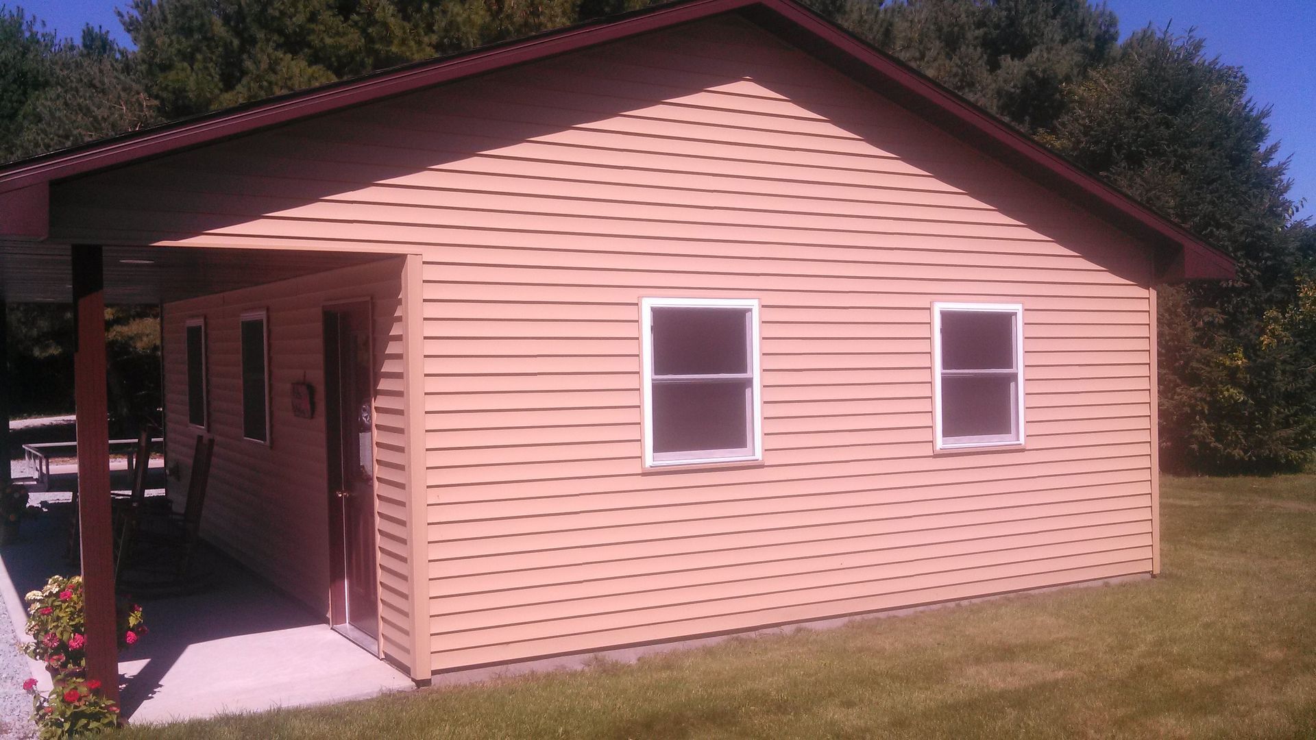 Pink house with a covered front porch, white windows, and a sloped roof on a grassy lot