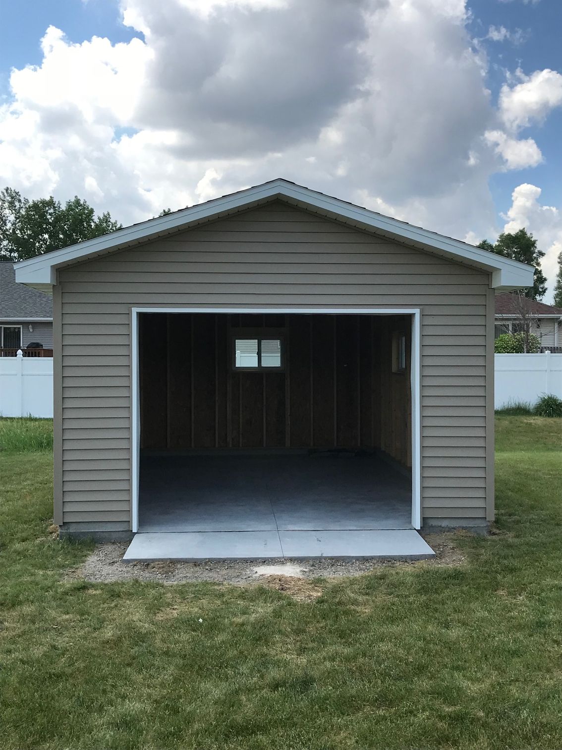 Small beige detached garage with an open front door and empty interior on a grassy yard.