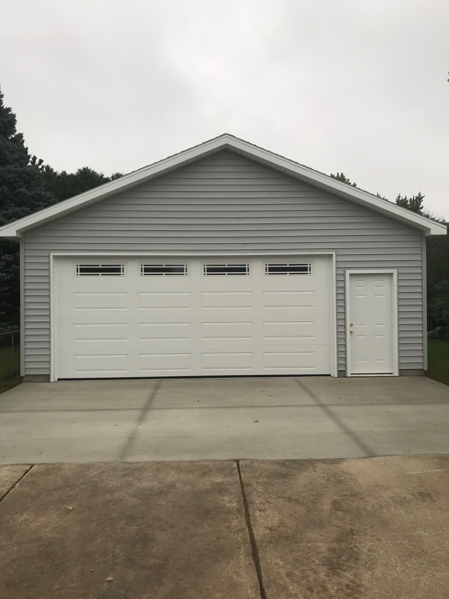 White three-car garage with side door and concrete driveway under an overcast sky