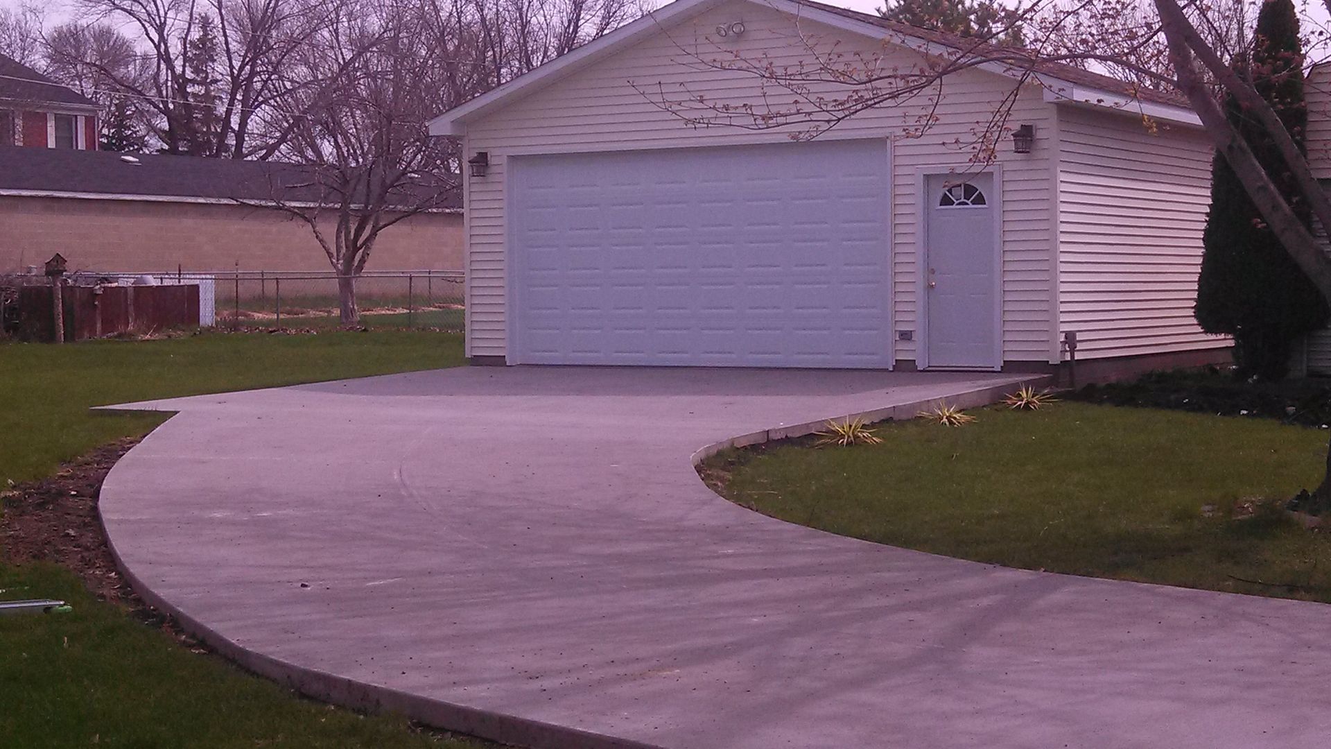 Suburban house with a white garage and curved concrete driveway under overcast skies.