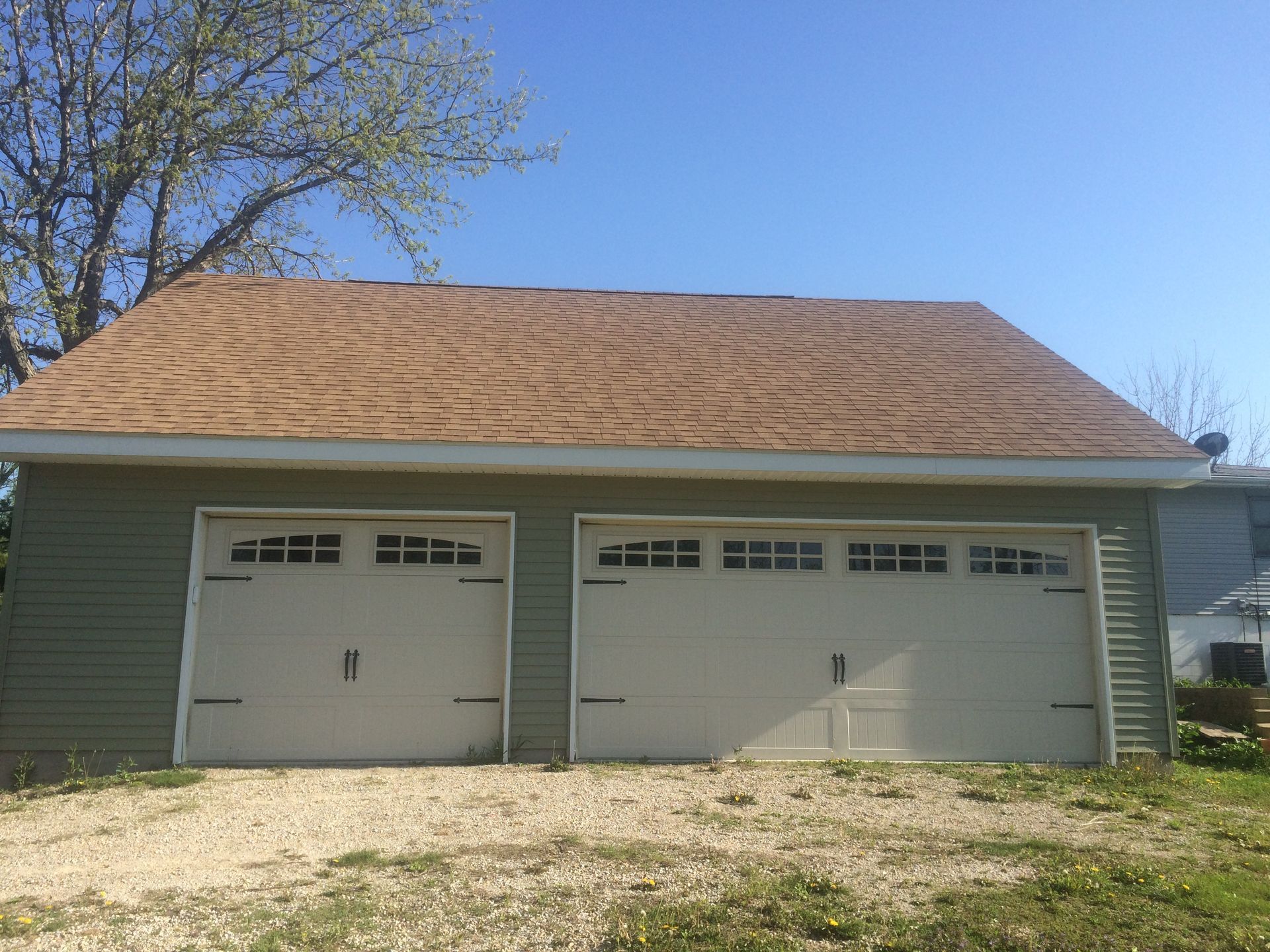 Two-car garage with white doors, tan siding, and a shingled roof under a blue sky