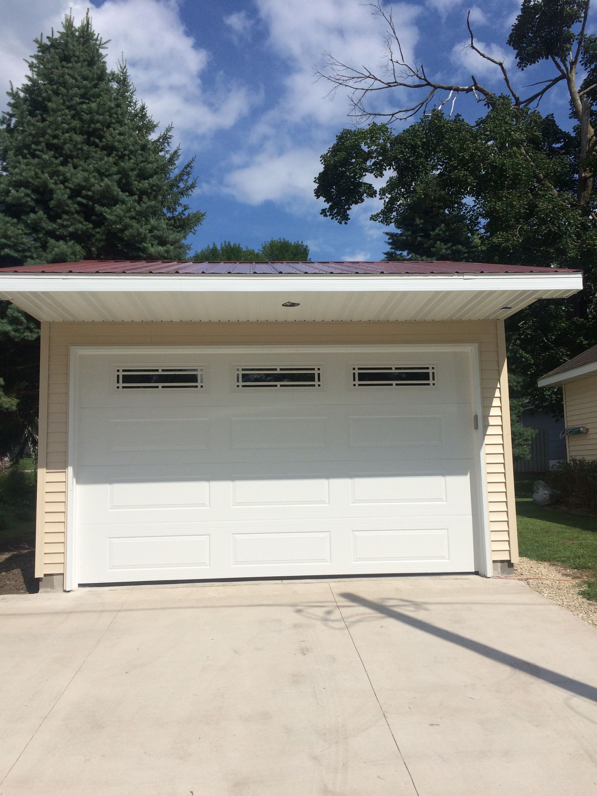 White garage door with small windows under a flat roof, set in a driveway with trees and blue sky.