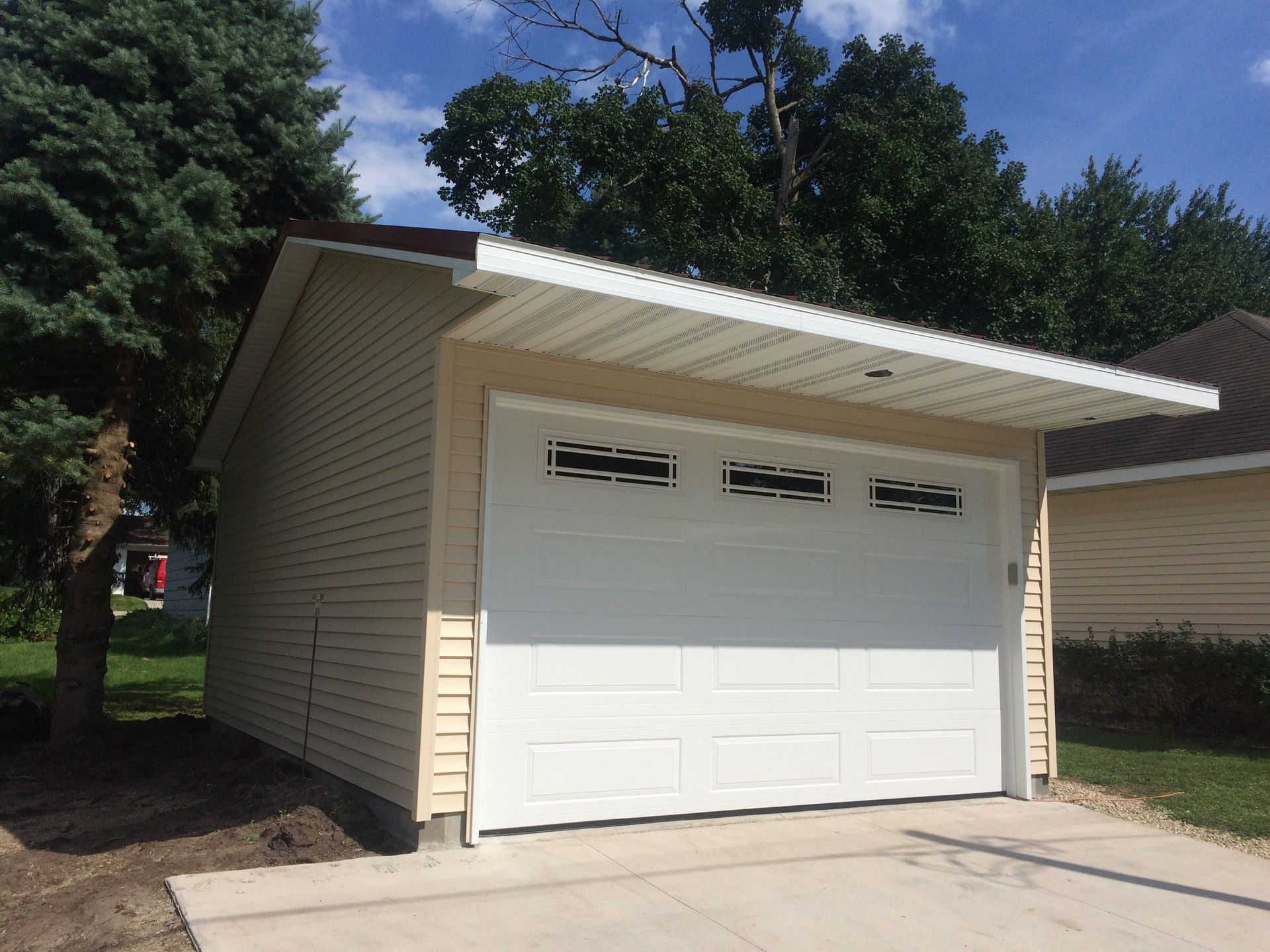 Beige detached garage with white door and sloped roof in a sunny residential yard