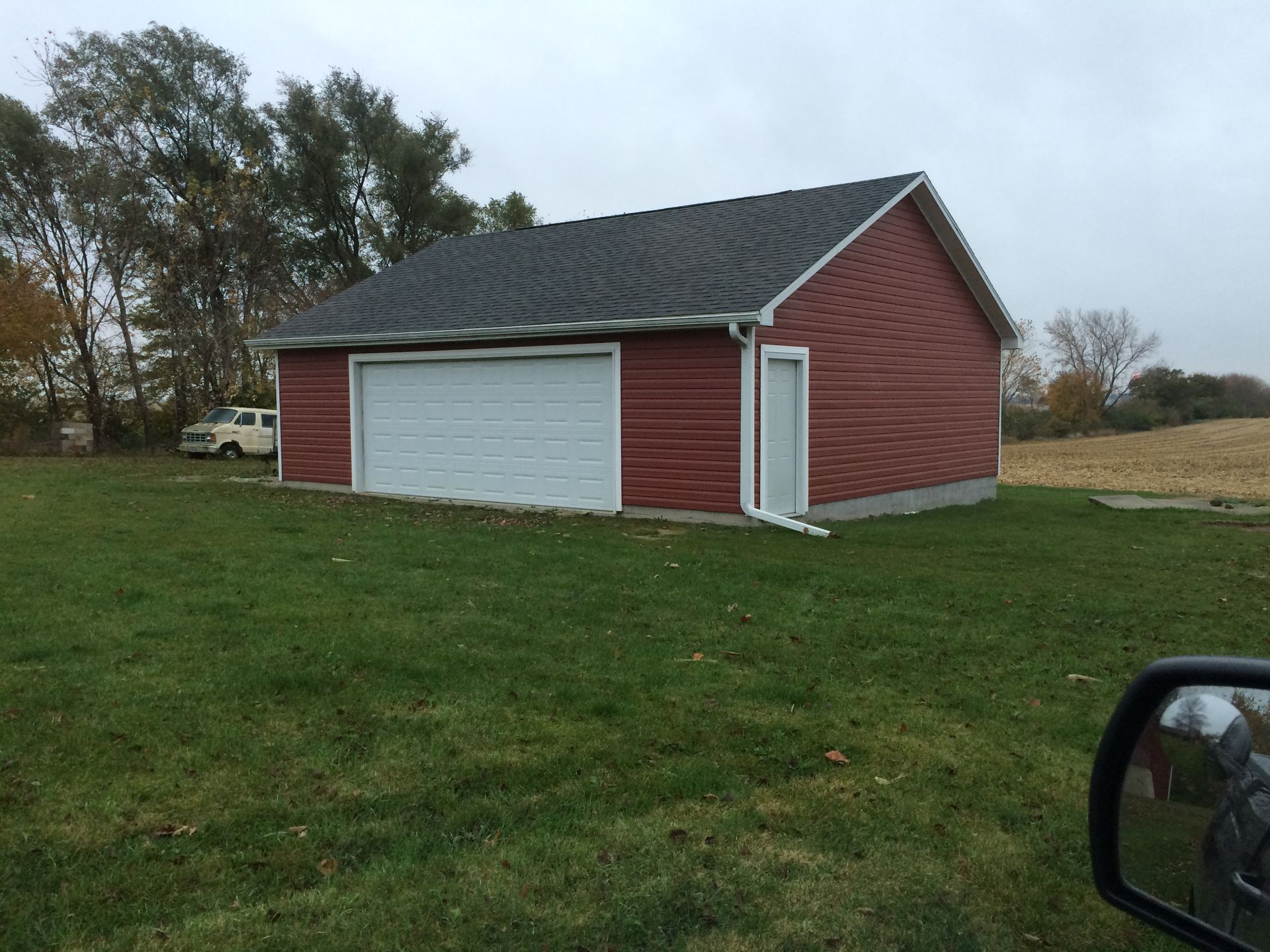 Red shed with white garage door and side entry door on a grassy lot under overcast skies.